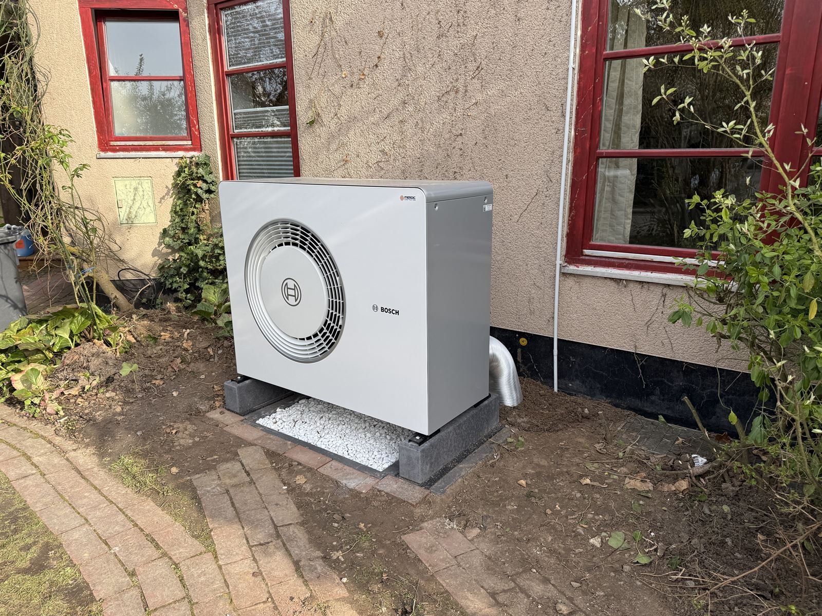 Bosch-Wärmepumpe auf Kiesbett vor dem Mehrfamilienhaus in Kassel, seitliche Ansicht