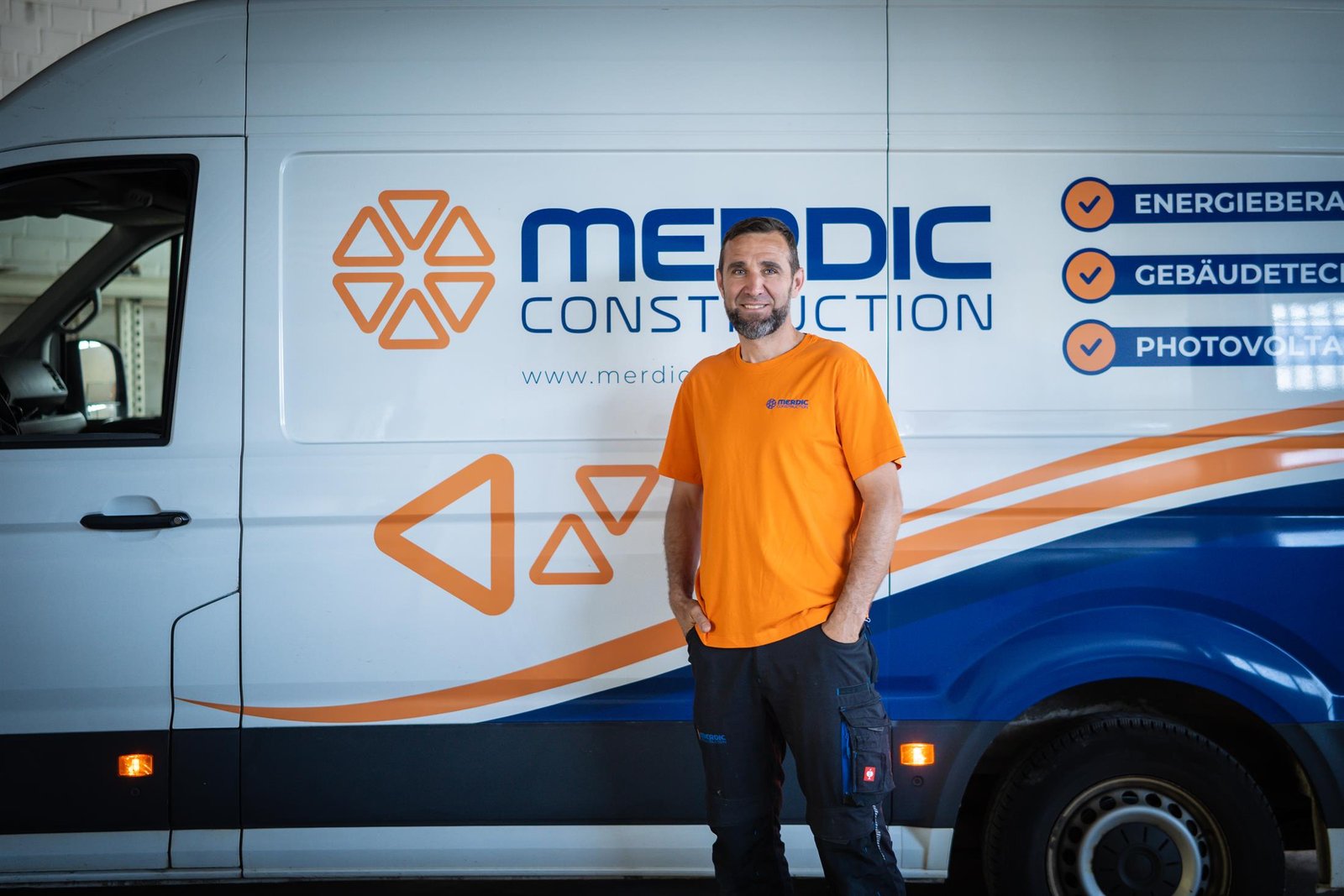 Monteur von Merdic Construction vor dem Firmenwagen mit Logo in Kassel