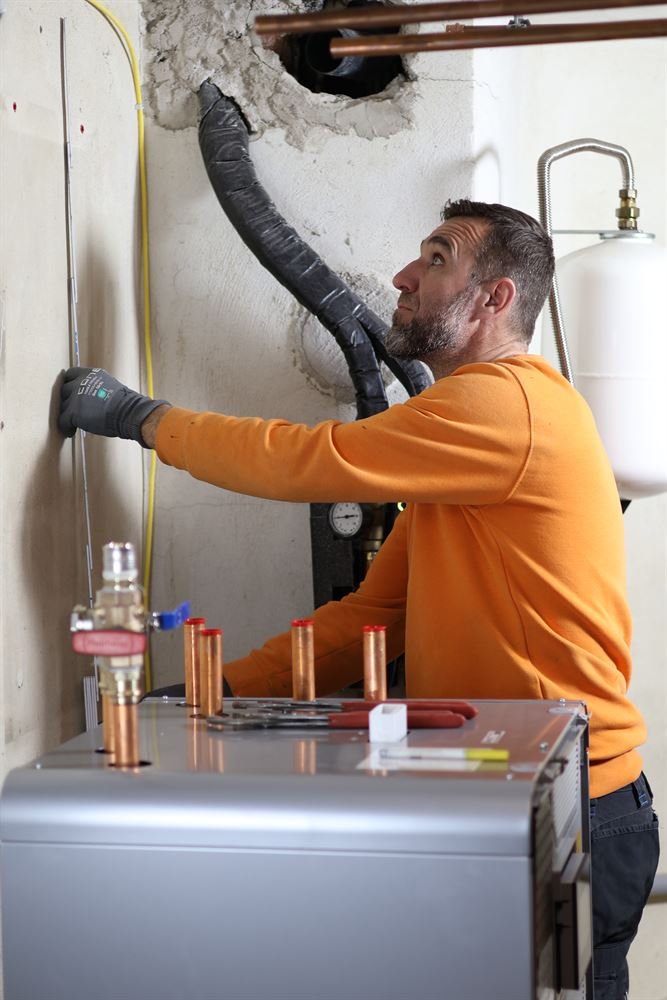 Monteur von Merdic Construction installiert die Inneneinheit einer Wärmepumpe im Heizungsraum