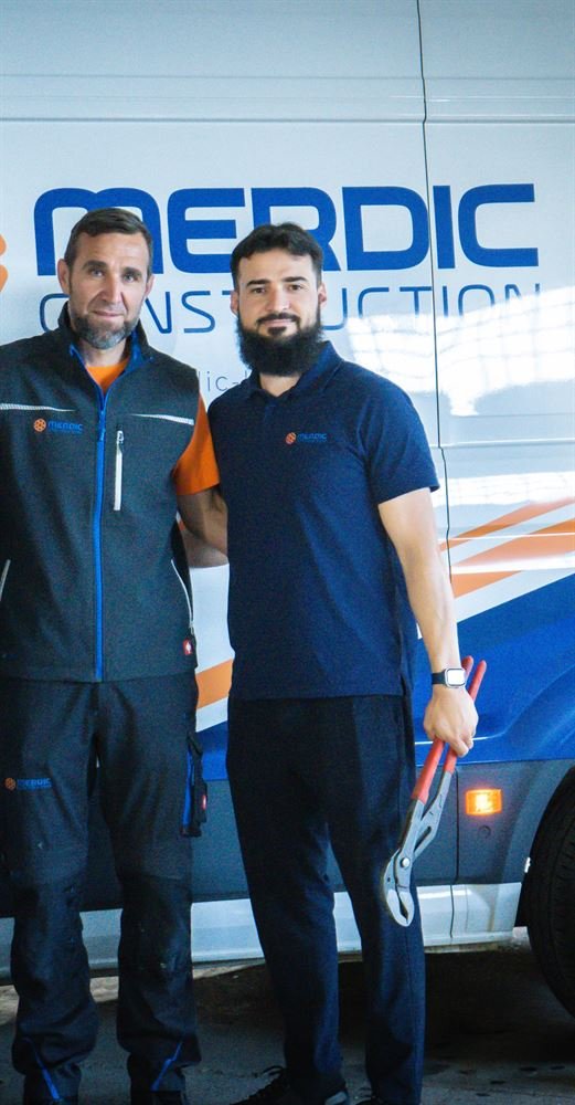 Zwei Mitarbeiter von Merdic Construction vor dem Firmenwagen mit Logo