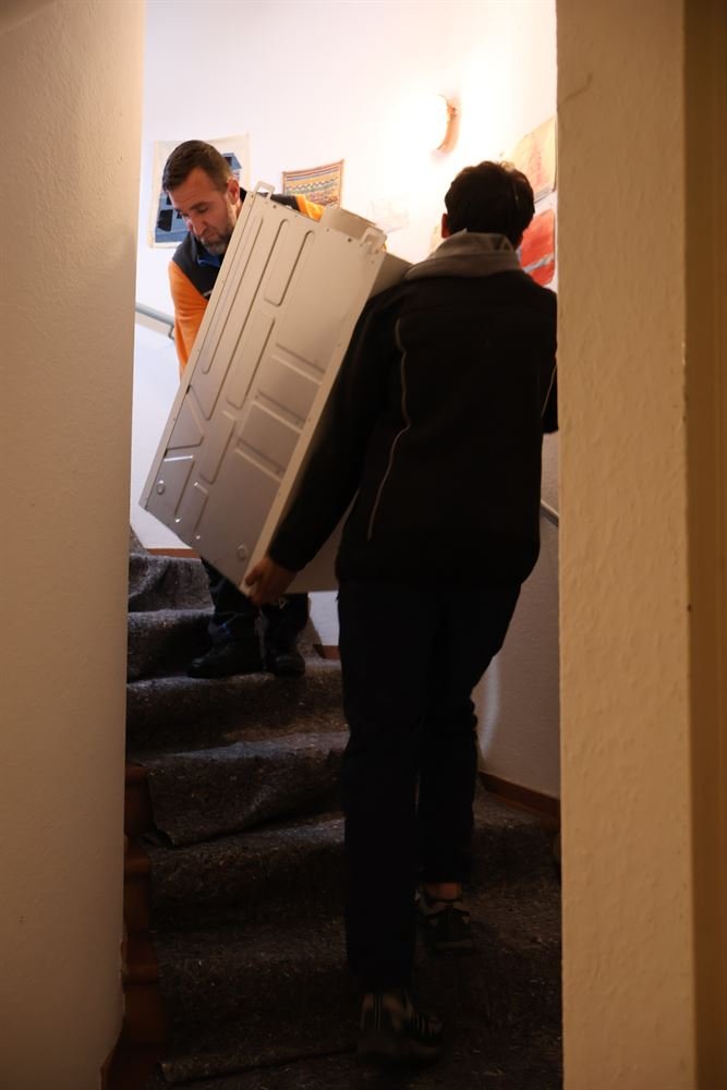 Zwei Mitarbeiter tragen die Inneneinheit einer Wärmepumpe die Treppe hinauf